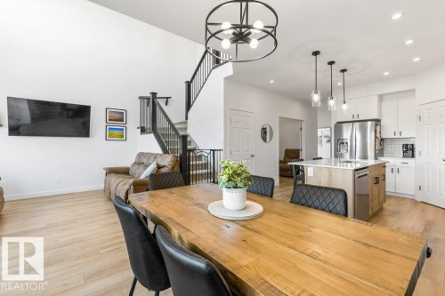 Open-concept living space featuring high ceilings, light wood-finish flooring, a contemporary black metal chandelier, a modern kitchen with a white subway tile backsplash, and a staircase with black metal railings - 25 Nettle Crescent, St. Albert, AB 