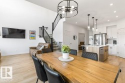 Open-concept living space featuring high ceilings, light wood-finish flooring, a contemporary black metal chandelier, a modern kitchen with a white subway tile backsplash, and a staircase with black metal railings - 