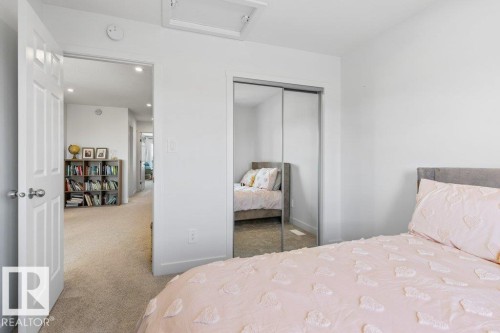 Interior bedroom featuring a sliding mirrored closet door, white walls, and a light-colored carpeted floor - 25 Nettle Crescent, St. Albert, AB 