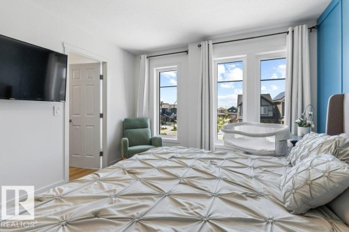 Bright bedroom featuring multiple large windows, wood-finish flooring, a paneled interior door, a light blue accent wall, and recessed ceiling lighting - 25 Nettle Crescent, St. Albert, AB 