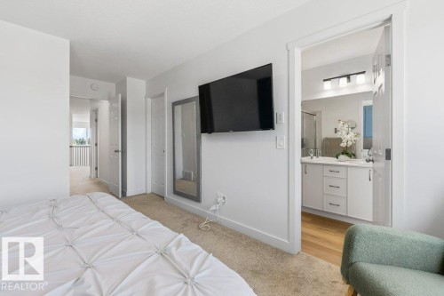 Carpeted sleeping area featuring white walls, a mounted mirror, and a doorway opening to a bathroom with a dual vanity, light wood-finish flooring, and a glass-enclosed shower - 25 Nettle Crescent, St. Albert, AB 