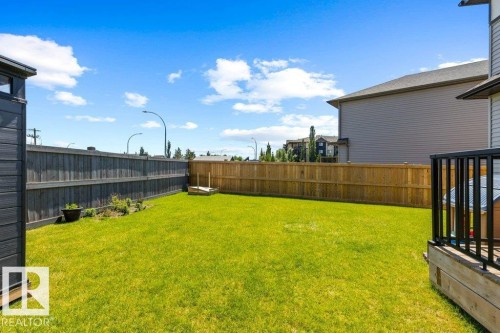 Expansive lawn area with perimeter fencing, a wooden deck with black railings, and a small garden bed - 25 Nettle Crescent, St. Albert, AB 