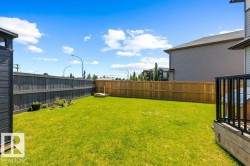 Expansive lawn area with perimeter fencing, a wooden deck with black railings, and a small garden bed - 