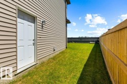 Side yard featuring a white entry door with overhead transom, tan horizontal siding, and a wooden privacy fence enclosing a grass lawn - 