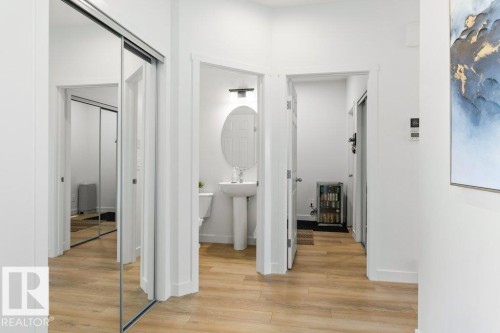 Hallway featuring wood-finish flooring, white walls, and a full-length mirrored sliding door - 25 Nettle Crescent, St. Albert, AB 