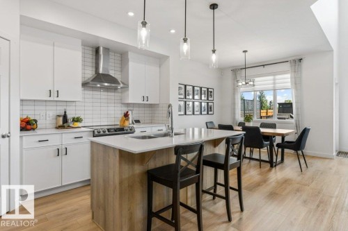 Open-concept kitchen featuring white cabinetry, a subway tile backsplash, stainless steel range hood, and an island with a light-toned countertop - 25 Nettle Crescent, St. Albert, AB 