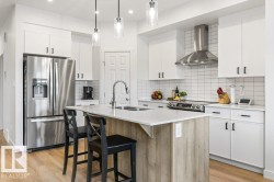 Contemporary kitchen featuring white cabinetry, stainless steel appliances, a white subway tile backsplash, a wood-finish island with a white countertop, and recessed lighting - 