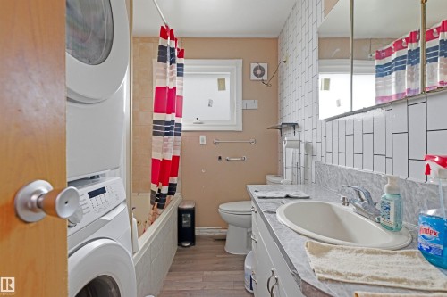 Bathroom featuring a white vanity with an integrated sink, a large wall-mounted mirror, and a stacked washer and dryer unit - 8911 169 Street Nw, Edmonton, AB 