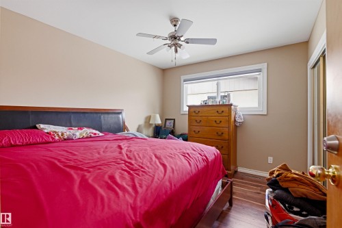 Bedroom featuring wood-finish flooring, a ceiling fan with integrated lighting, a window with white trim, and a sliding mirrored closet door - 8911 169 Street Nw, Edmonton, AB 