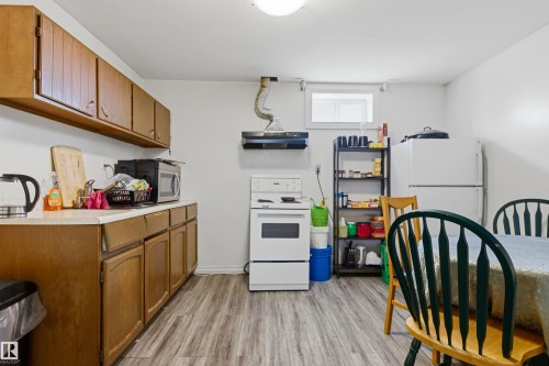 Kitchen featuring wood cabinetry, light-toned countertops, wood-finish flooring, a white range, and a white refrigerator - 8911 169 Street Nw, Edmonton, AB 