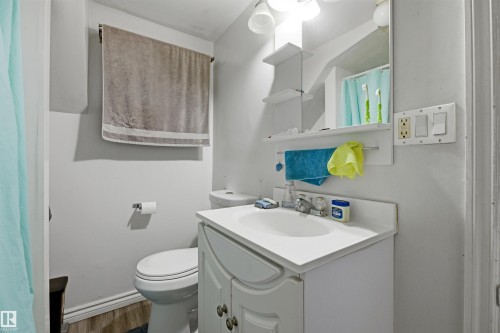 Bathroom featuring a white vanity with integrated sink, wood-finish flooring, and wall-mounted mirror with integrated shelving - 8911 169 Street Nw, Edmonton, AB 