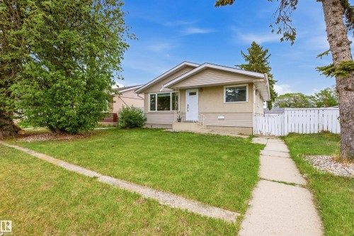 Ranch-style exterior with tan stucco and horizontal siding, featuring a front lawn, mature trees, and a concrete walkway - 8911 169 Street Nw, Edmonton, AB 