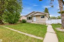 Ranch-style exterior with tan stucco and horizontal siding, featuring a front lawn, mature trees, and a concrete walkway - 8911 169 Street Nw, Edmonton, AB 