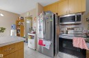 Kitchen featuring wood-finish cabinetry, stainless steel appliances including a refrigerator and range with an overhead microwave, and light-toned floor tiling - 8911 169 Street Nw, Edmonton, AB 
