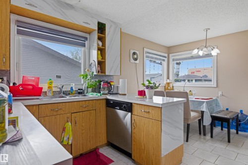 Kitchen and dining area featuring a double basin stainless steel sink, wood-finish cabinetry, light-toned countertops, and tiled flooring - 8911 169 Street Nw, Edmonton, AB 