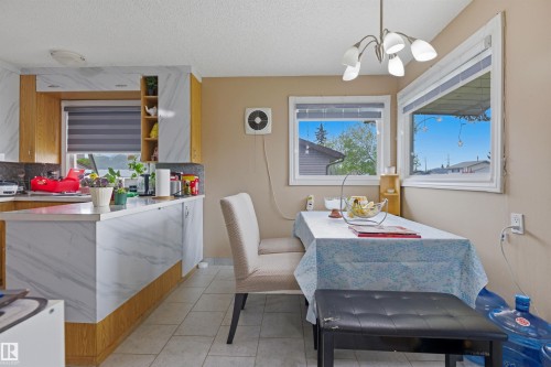 Kitchen and dining area featuring wood-finish cabinetry with white and grey marbled surfaces, white tile flooring, and a multi-light ceiling fixture - 8911 169 Street Nw, Edmonton, AB 