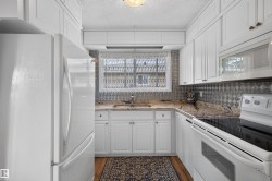 Galley kitchen with white cabinetry, patterned backsplash, light-colored countertops, stainless steel sink, and built-in appliances - 