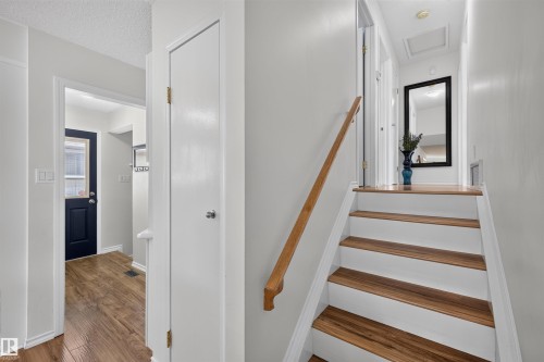 Interior hallway featuring wood-finish flooring, white walls, and a wooden handrail alongside a staircase with white risers and wood-finish treads - 244 Knottwood Road N, Edmonton, AB 