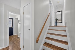 Interior hallway featuring wood-finish flooring, white walls, and a wooden handrail alongside a staircase with white risers and wood-finish treads - 