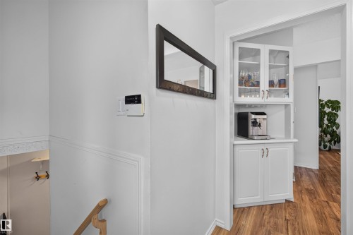 Built-in beverage station featuring white cabinetry, glass-front upper cabinets, and wood-finish flooring - 244 Knottwood Road N, Edmonton, AB 
