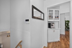 Built-in beverage station featuring white cabinetry, glass-front upper cabinets, and wood-finish flooring - 