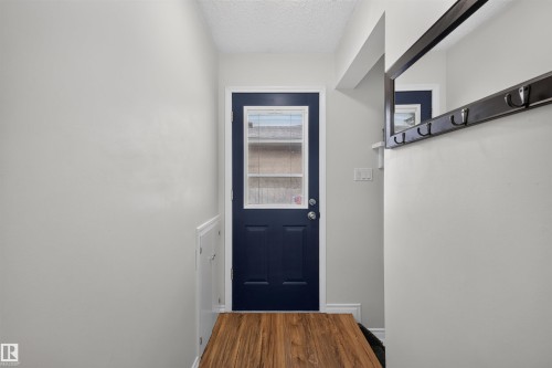 Entryway featuring wood-finish flooring, a navy blue door with integrated window panels, light gray walls, and a mounted mirror with coat hooks - 244 Knottwood Road N, Edmonton, AB 
