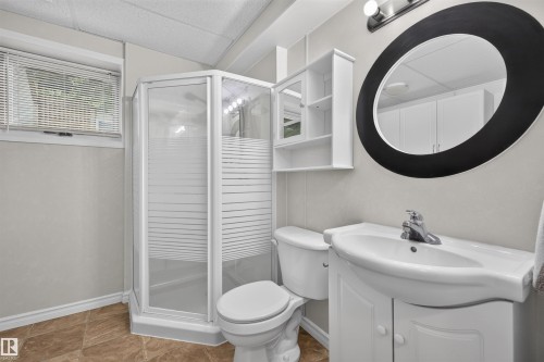 Three-piece bathroom featuring a corner shower with a glass enclosure, a white vanity with an integrated sink, a wall-mounted storage cabinet, and a large oval mirror - 244 Knottwood Road N, Edmonton, AB 