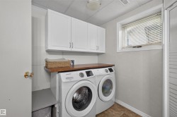 Laundry area featuring white cabinetry, a wood-finish countertop, and a window with blinds - 