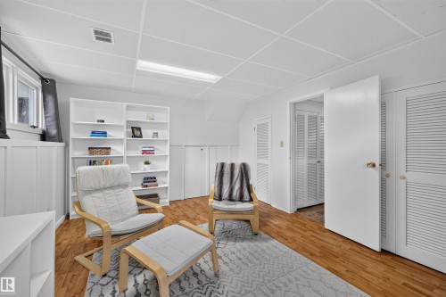 Room featuring wood-finish flooring, white built-in shelving, white paneled walls, and white louvered closet doors - 244 Knottwood Road N, Edmonton, AB 