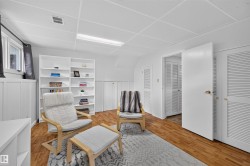 Room featuring wood-finish flooring, white built-in shelving, white paneled walls, and white louvered closet doors - 