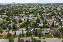 Aerial perspective of a residential street featuring a single-family dwelling with a dark shingled roof and light gray siding - 
