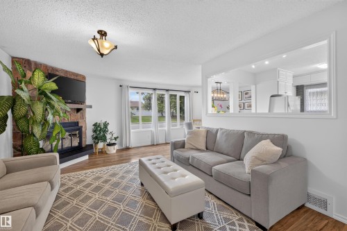 Living area featuring wood-finish flooring and a stone-clad fireplace with a black mantel - 244 Knottwood Road N, Edmonton, AB 