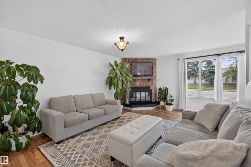 Living area featuring a corner stone-faced fireplace with a black hearth, wood-finish flooring, white walls, and a large window with white trim - 244 Knottwood Road N, Edmonton, AB 