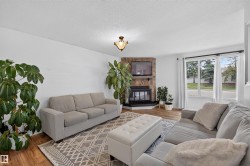 Living area featuring a corner stone-faced fireplace with a black hearth, wood-finish flooring, white walls, and a large window with white trim - 