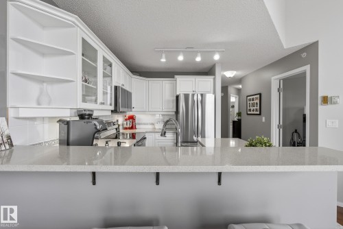 Modern kitchen featuring white cabinetry, stainless steel appliances, a breakfast bar with a light-toned countertop, and track lighting - 421 9730 174 Street, Edmonton, AB 