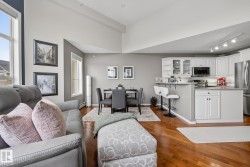 Open-concept living area featuring high vaulted ceilings, large windows, wood-finish flooring, a dining space, and a kitchen with white cabinetry and stainless steel appliances - 