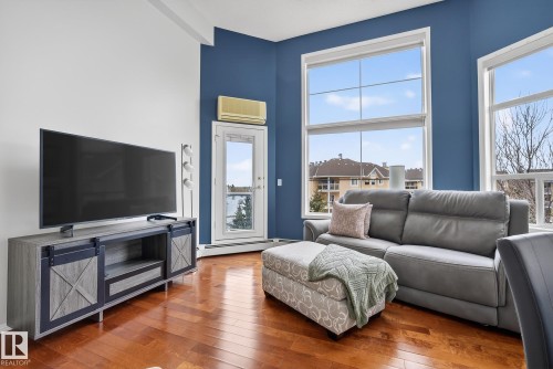 Living area featuring wood-finish flooring, high ceilings, large multi-pane windows, and a glass-paneled door - 421 9730 174 Street, Edmonton, AB 
