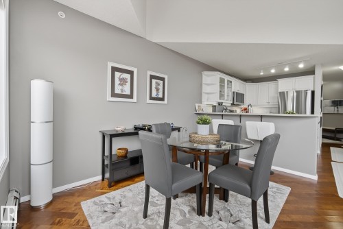 Open-concept dining area featuring wood-finish flooring, a kitchen pass-through with breakfast bar seating, white cabinetry, and stainless steel appliances - 421 9730 174 Street, Edmonton, AB 