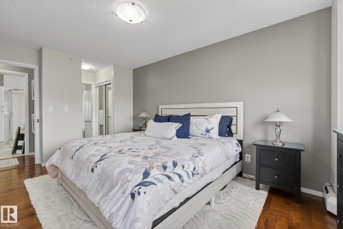 Bedroom featuring wood-finish flooring, a contemporary ceiling light fixture, and an en-suite bathroom with a glass-enclosed shower - 421 9730 174 Street, Edmonton, AB 