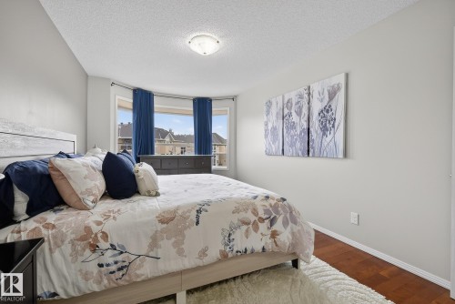 Bedroom featuring a prominent bay window with exterior views, hardwood flooring, neutral wall tones, and a ceiling-mounted light fixture - 421 9730 174 Street, Edmonton, AB 