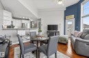 Open-concept living space featuring wood-finish flooring, a contemporary ceiling fan, and a kitchen bar with white cabinetry and stainless steel appliances - 421 9730 174 Street, Edmonton, AB 