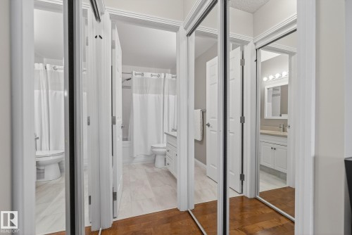 Mirrored closet doors revealing two distinct bathrooms, each featuring a white vanity with a countertop and a wall-mounted light fixture - 421 9730 174 Street, Edmonton, AB 