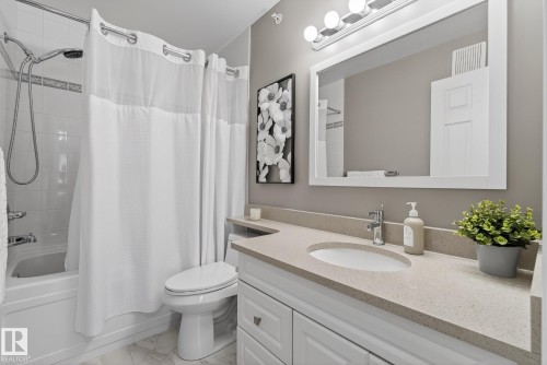 Bathroom featuring a vanity with an integrated sink and light-toned countertop, white paneled cabinetry, and a framed mirror - 421 9730 174 Street, Edmonton, AB 