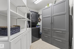 Laundry room with a stacked washer and dryer, white open shelving, white lower cabinetry, and gray closed cabinetry with drawers - 