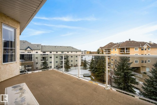 Outdoor balcony featuring glass panel railings, a textured stucco exterior, and a large window - 421 9730 174 Street, Edmonton, AB 