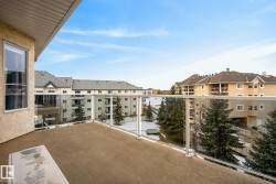 Outdoor balcony featuring glass panel railings, a textured stucco exterior, and a large window - 
