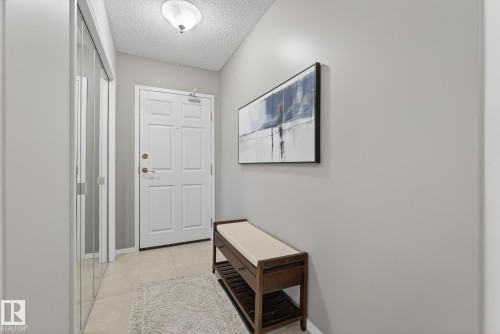 Entryway featuring a paneled door with brass hardware, tile flooring, and mirrored closet doors - 421 9730 174 Street, Edmonton, AB 