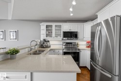 U-shaped kitchen featuring stone countertops, stainless steel appliances, white cabinetry with glass-front uppers, and a double basin sink with a gooseneck faucet - 