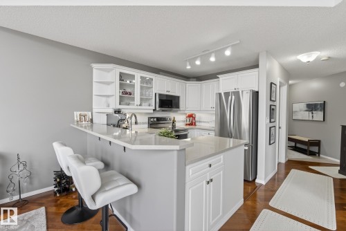 Kitchen featuring white cabinetry, stainless steel appliances, a breakfast bar, and wood-finish flooring - 421 9730 174 Street, Edmonton, AB 