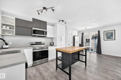 Contemporary kitchen featuring white and gray cabinetry, stainless steel appliances, and a butcher block island - 